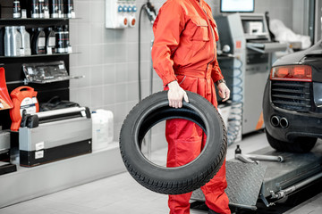 Wall Mural - Car service worker in red uniform carrying new tires at the tire mounting service or shop