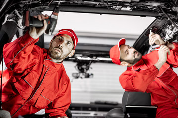 Wall Mural - Two auto service workers in red uniform disassembling new car interior making some improvements indoors