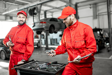 Portrait of a two handsome auto mechanics in red uniform standing with working tools at the car service