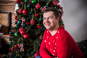 Smiling young man at Christmas time near christmas tree and gift at home. Holidays and vacation  