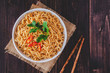 Cooked instant noodles in bowl with chopsticks in top view closeup on wooden table with copy space