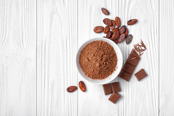 Wall Mural - Top view of cocoa powder and beans with broken chocolate bar on white wooden background