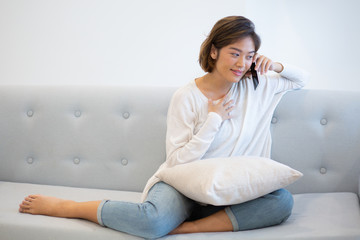 Wall Mural - Portrait of smiling young woman talking on phone to friend. Asian girl sitting on coach and using smartphone at home. Wireless communication concept