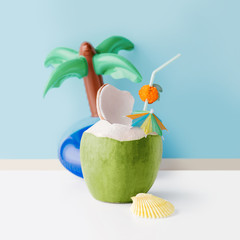 Wall Mural - Fresh coconut on a pastel blue background with coconut tree inflatable drink holder, summer vibes concept