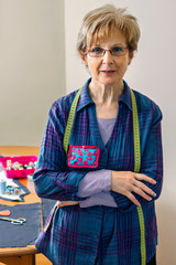 Wall Mural - Senior dressmaker posing looking at camera with table with sewing materials in the background