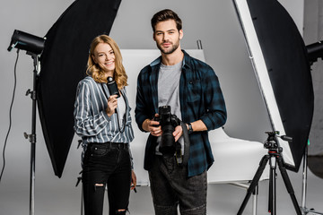 young photographers with professional equipment standing together and smiling at camera in photo studio