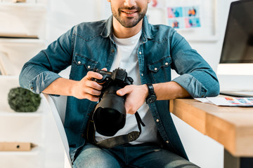 Wall Mural - cropped shot of smiling young photographer holding camera at workplace