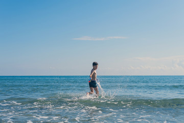 Wall Mural - Happy teen boy with snorkeling mask and tube running оn the wave of the sea during summer vacation in the tropical resort town