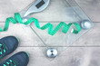 © taniasv - Green measure tape, glass weighing scale, running shoes on a rustic surface. Weight management and healthy wellbeing concept in flat lay