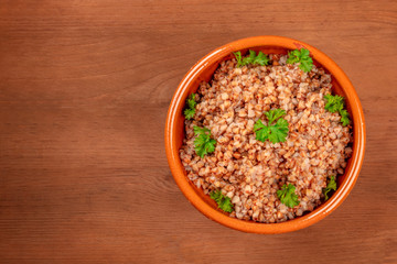 Cooked buckwheat in an earthenware bowl, garnished with fresh parsley leaves, on a dark rustic wooden table with copy space