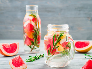 infused detox water with grapefruit and rosemary in mason jar and glass bottle on gray wooden table. diet healthy eating and weight loss concept, copy space for text