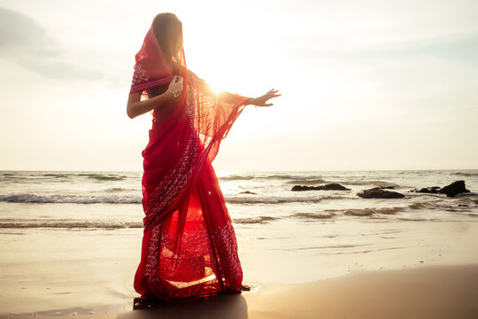 indian female model in vacation on paradise tropical beach by ocean sea. hindu woman with kundan jewelry traditional India costume red wedding sari.asian girl near the rocks shores of Indian Ocean bay