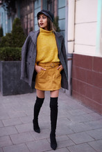 beautiful fashionable woman in bright yellow sweater and skirt and knee high heel boots walking and posing outdoors