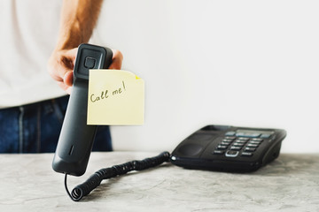 Man holds handset with paper with handwritten inscription call me near concrete table with old telephone on white background. Communication concept. Copy space