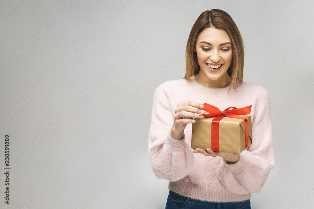 Obraz na płótnie Image of Happy brunette woman in casual holding gift box and looking at the camera isolated over white background. w salonie
