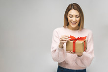 Image of Happy brunette woman in casual holding gift box and looking at the camera isolated over white background.