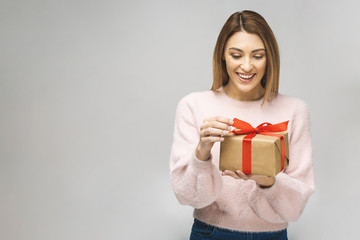 Wall Mural - Image of Happy brunette woman in casual holding gift box and looking at the camera isolated over white background.