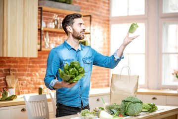 Handsome man throwing up green pepper while cooking vegan meals on the kitchen at home