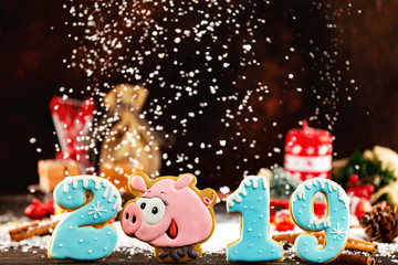 Wall Mural - Gingerbread funny smiling pig and numbers as a symbol of happy new 2019 year at xmas decorated with fir cones and candles background with falling snow. Merry christmas greeting card.