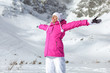 © Lubo Ivanko - Young woman in pink ski jacket, gloves and pants, arms spread, eyes closed, smiling facing sun, snow covered mountain behind her.