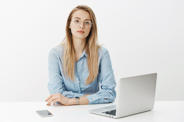 Wall Mural - Time is money. Bossy self-assured successful female entrepreneur in blue-collar shirt and glasses sitting near laptop, glasses with trendy watches on arm looking serious at camera ready for business