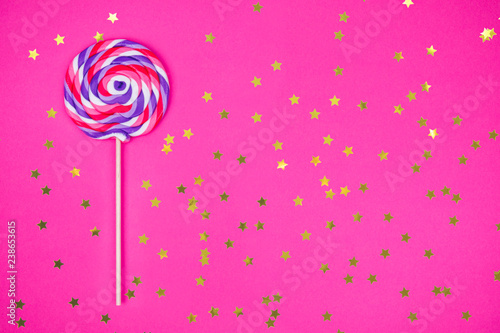 Photographie Big lollipop on solid pink background with golden sprinkles