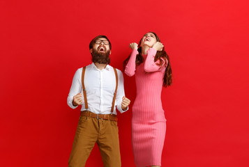 Wall Mural - young happy couple won emotionally celebrating win on colored red background.