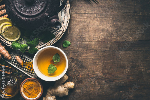 Herbal turmeric tea background. Cup of healthy turmeric spice tea with iron teapot and ingredients:  lemon,  ginger, cinnamon sticks and honey , top view with copy space. Immune boosting remedy