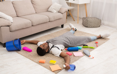 Wall Mural - Tired man lying on carpet surrounded by cleaning supplies