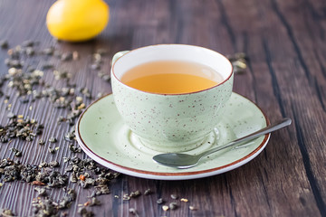 Cup of green tea, lemon and leaves of dry green tea on a brown wooden table. Superfood concept.