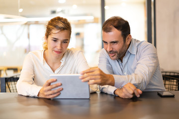 Wall Mural - Portrait of happy colleagues browsing on digital tablet at cafe. Young Caucasian businesswoman and mid adult businessman communicating at break. Wireless technology concept