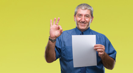 Canvas Print - Handsome senior man holding blank sheet paper over isolated background doing ok sign with fingers, excellent symbol