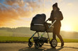 Walking woman with baby stroller at sunset.