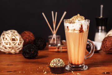 Wall Mural - Beautifully decorated latte macchiato coffee with whipped cream and sprinkled with crushed halva, in high transparent glass, on a wooden table, on a dark background