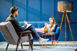 Young woman visiting male psychologist lying on the comfortable couch during psychological session in the luxury blue office interior