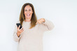 © Krakenimages.com - Middle age woman using smartphone over isolated background with surprise face pointing finger to himself