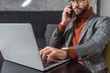 © LIGHTFIELD STUDIOS - cropped view of handsome businessman in glasses and formal wear sitting at table, talking on smartphone and typing on laptop in restaurant