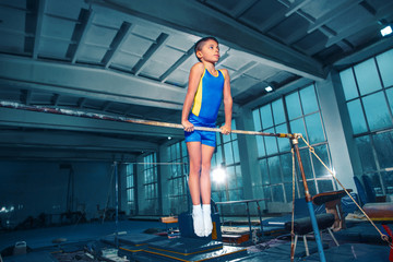 Wall Mural - The little boy is engaged in sports gymnastics on a parallel bars at gym. The performance, sport, acrobat, acrobatic, exercise, training concept