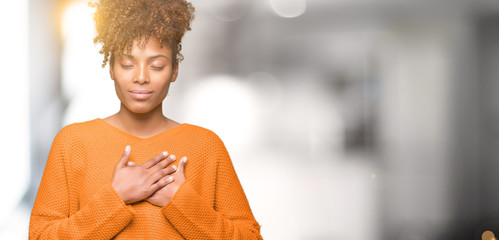 Wall Mural - Beautiful young african american woman over isolated background smiling with hands on chest with closed eyes and grateful gesture on face. Health concept.