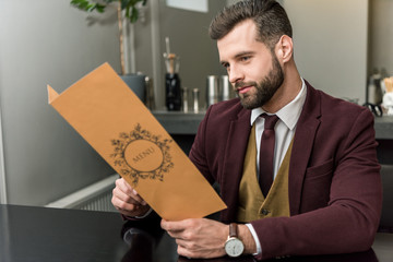 handsome businessman in formal wear sitting at restaurant and holding menu