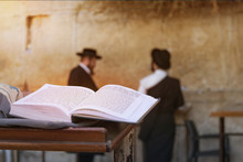 Jewish Bible On Table, Wailing Western Wall, Jerusalem, Israel. Book Of The Torah-the Pentateuch Of Moses Is Open On The Prayer Table On The Background Of Praying Orthodox Jews