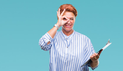 Canvas Print - Senior caucasian business woman holding clipboard over isolated background with happy face smiling doing ok sign with hand on eye looking through fingers