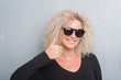 © Krakenimages.com - Young blonde woman with curly hair over grunge grey background doing happy thumbs up gesture with hand. Approving expression looking at the camera with showing success.