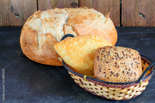 Fotografía Loaf of bread and the buns on the dark rustic background.