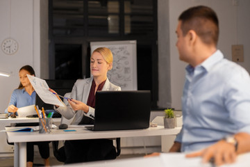 Poster - business, deadline and technology concept - woman showing charths to colleague late at night office