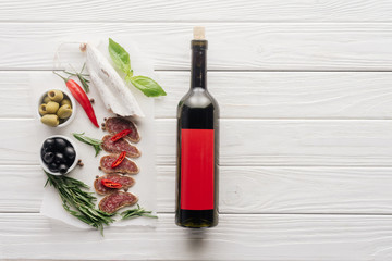 Wall Mural - top view of bottle of red wine and assorted meat snacks on white wooden tabletop