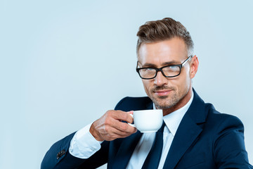 Wall Mural - handsome businessman drinking coffee and looking at camera isolated on white