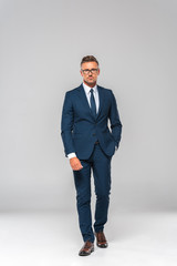 Wall Mural - handsome businessman in suit and glasses walking and looking at camera isolated on white