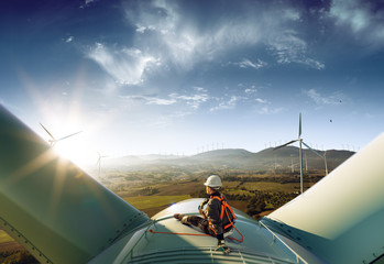 Happy engineer feel success after good work. He standing a top of windmill and looking beautiful sunset