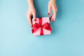 Wall Mural - Overhead view on female hands with pink gift box wrapped with red bow on blue background. Minimal styled composition.